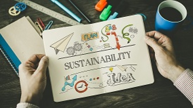 Zwei Hände halten ein aufgeschlagenes Papierheft mit über zwei Seiten gehender Schrift Sustainability