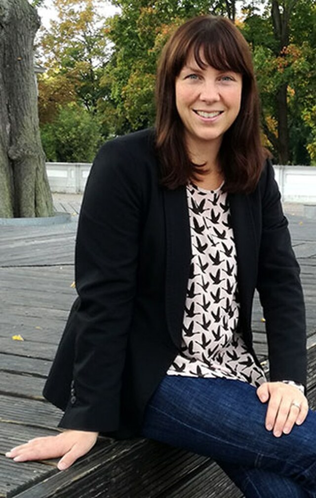 Christiane Bonk, sitzend auf einem Holzuntergrund, lächelt zugewandt in die Kamera. 