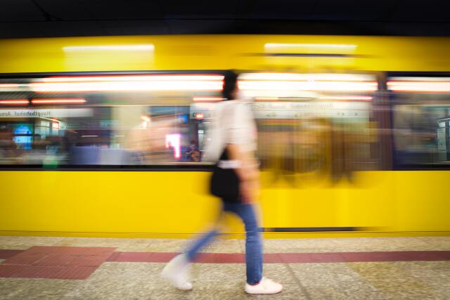 Straßen-/U-Bahn fährt durch U-Bahnstation, davor läuft eine Person entlang, Langzeitaufnahme mit Bewegungsunschärfe