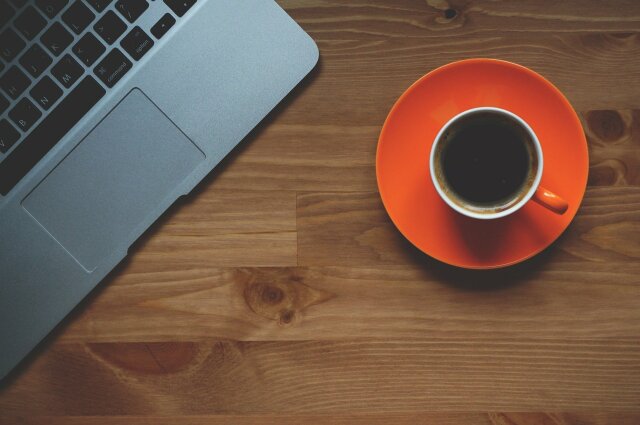 Foto aus Vogelperspektive (in der Nahen) von einer Tasse Kaffee und eines Laptops, die auf einem Holztisch sind.