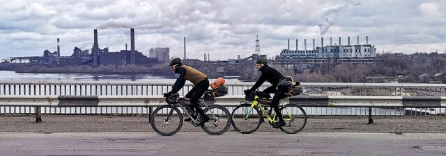 Foto der beiden Rennradler, die hintereinander über eine Brücke fahren.