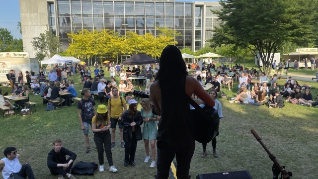 Foto eines Auftritts hinter dem HSZ aus Sicht der Bühne hinter Künstlerin, die eine Gitarre hält. 