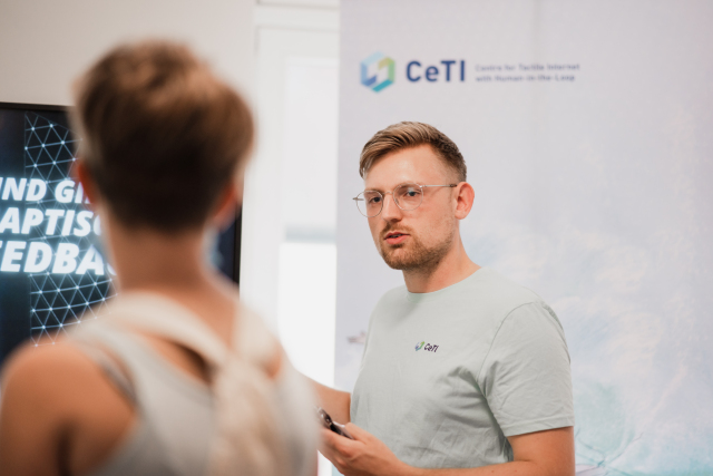 Foto, junger Mann und junge Frau sprechen miteinander, im Hintergrund ein Banner mit dem CeTI-Logo