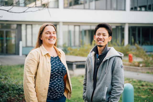 Foto Dr. Anna Poetsch und Dr. Tomohisa Toda, stehen nebeneinander. Sie befinden sich im Freien, auf einer grünen Wiese. Im Hintergrund ein Gebäude.