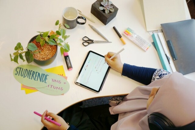 Foto: Blick von oben, Studierende schreibt mit Stift auf Tablet, neben dem Tablet liegen Schreibutensilien