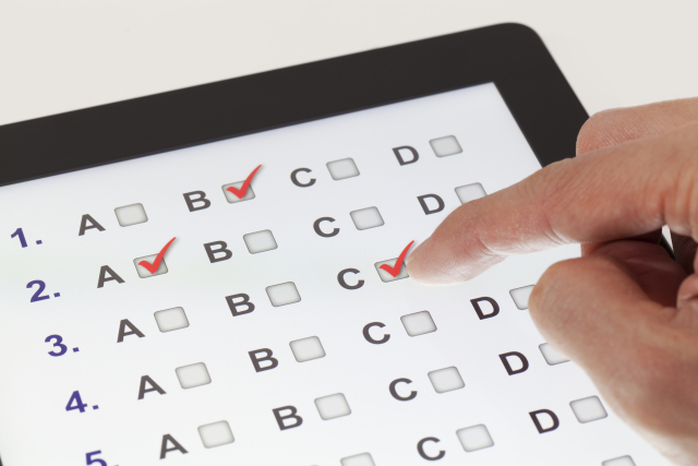 Foto: Tablet, auf dem der Antwortbogen zu einem Test dargestellt wird. Dabei muss man bei einem der Buchstaben von A bis D ein Häkchen setzen. Man erkennt außerdem die Hand einer Person, die einen Haken bei C setzt.