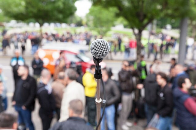 Mikrofon im Vordergrund und demonstrierende Personen verschwommen im Hintergrund