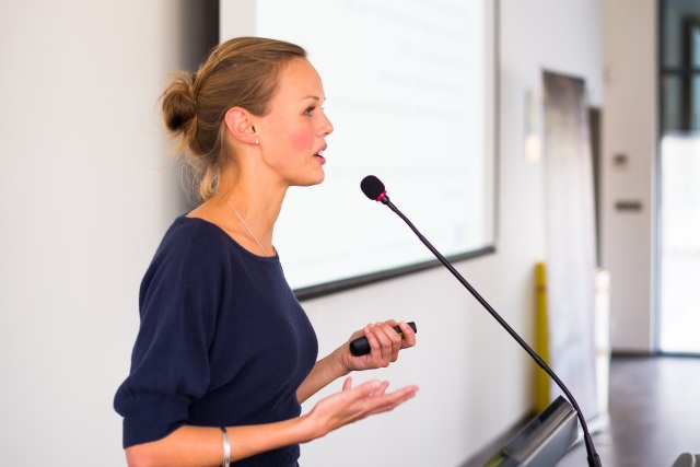 Junge Frau spricht an einem Rednerpult in ein Mikrofon
