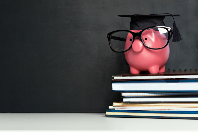 Pink piggy bank with glasses and doctor hat on dark background on pile of notebooks