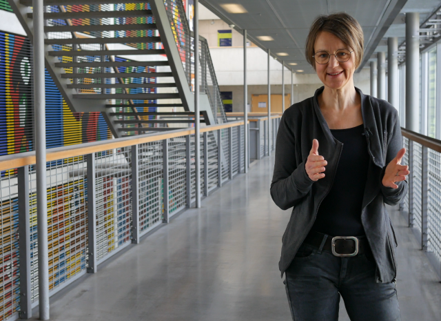 Das Foto zeigt Frau Sandra Buchmüller im Hörsaalzentrum. Im Hintergrund befinden sich Treppenaufgang und buntes Wandgemälde.