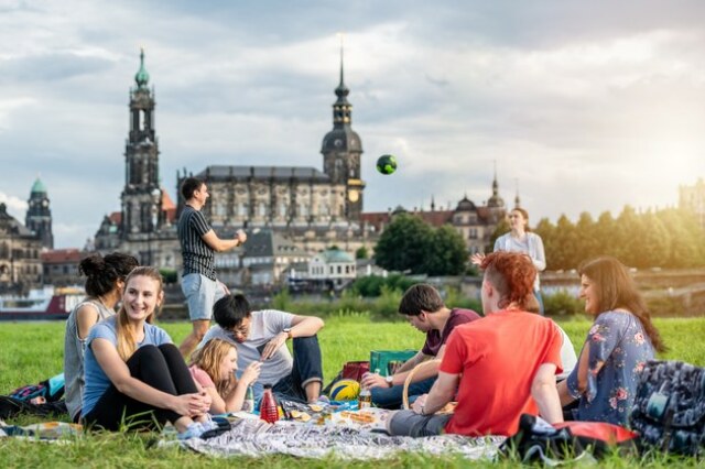 Panorama von Dresden von der Elbe aus mit Blick auf die Altstadt. Auf der Wiese ist eine Gruppe von sich unterhaltenden und spielenden Menschen.