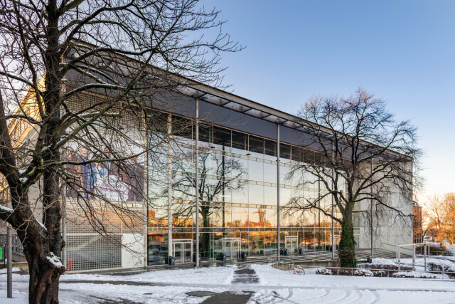 Das Foto zeigt eine Außenansicht des Hörsaalzentrums der TU Dresden. Auf den Wegen liegt Schnee, die Bäume tragen keine Blätter.