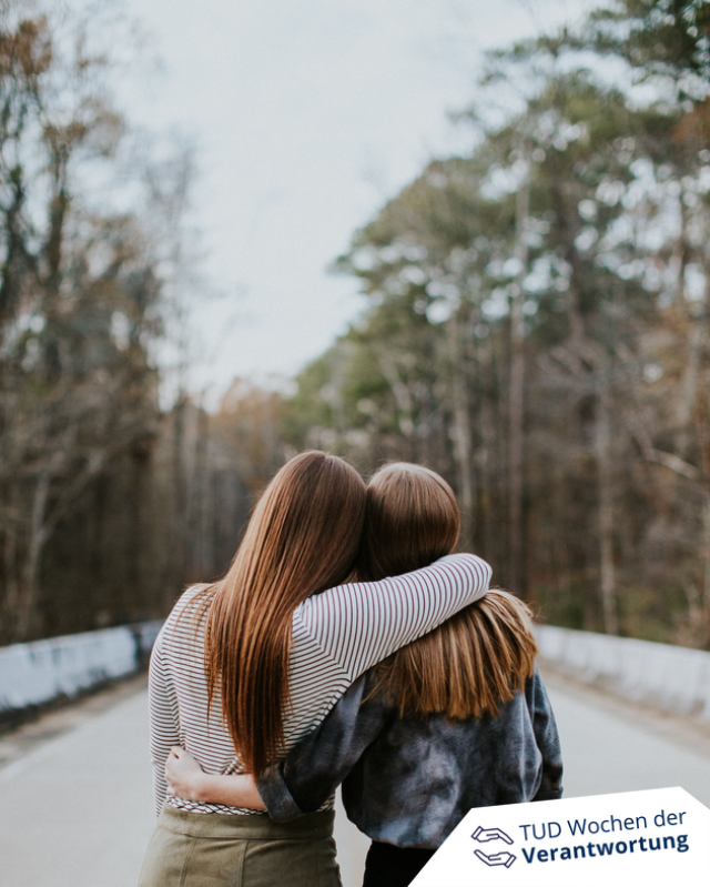  Zwei Frauen stehen mit dem Rücken zur Kamera und umarmen sich im Wald.