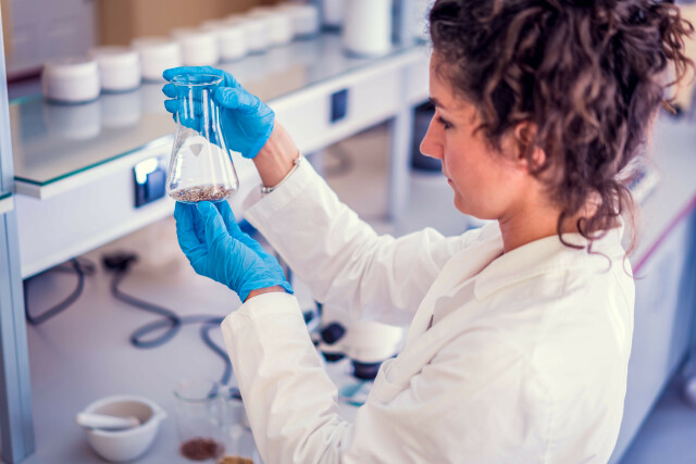 Foto im Labor, Studentin im weißen Kittel hält Erlenmeyerkolben in der Hand.