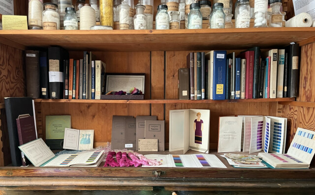 The photo shows a shelf with lots of books. There are many bottles on the shelf.