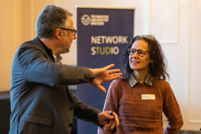 Two participants of the event in conversation, in the background a stand with the inscription 'NETZWERKSTUDIO'