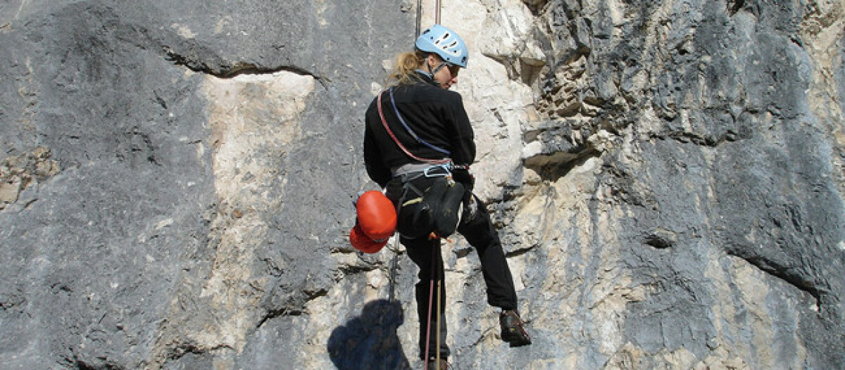 Eine jungen Frau mit kompletter Kletterausrüstung an einer Steilwand