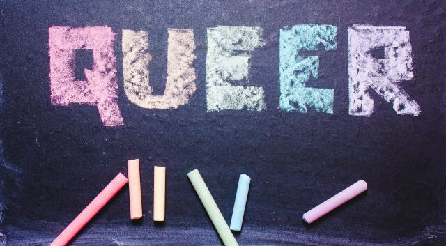 The photo shows a blackboard with the word QUEER written on it in several colours