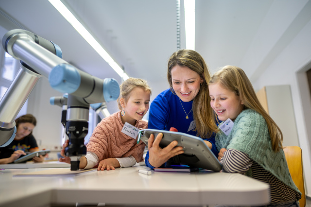 mother with two daughters using a tablet to move a robotic arm