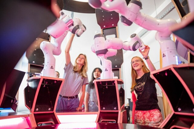 Schülerinnen stehen um einen kreisförmigen Tisch und hantieren mit roboterartigen Maschinen.