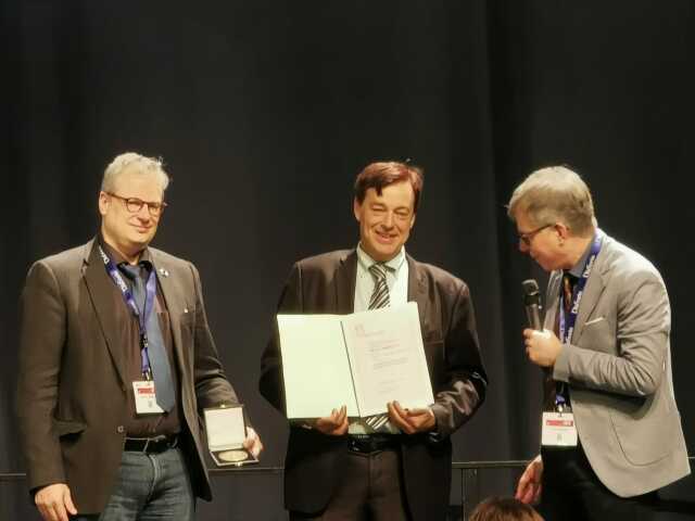 Photo shows 3 men at the award ceremony: Prof. Bornstein (center) holds certificate in his hand.