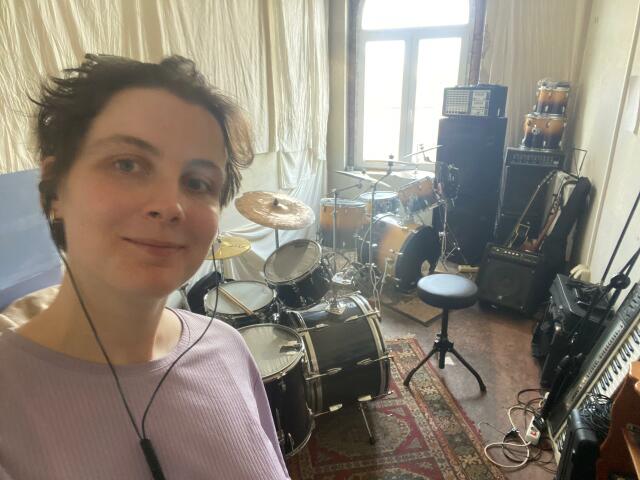 Photo of Leonie Reuter. She is standing in a rehearsal room with two drum sets.