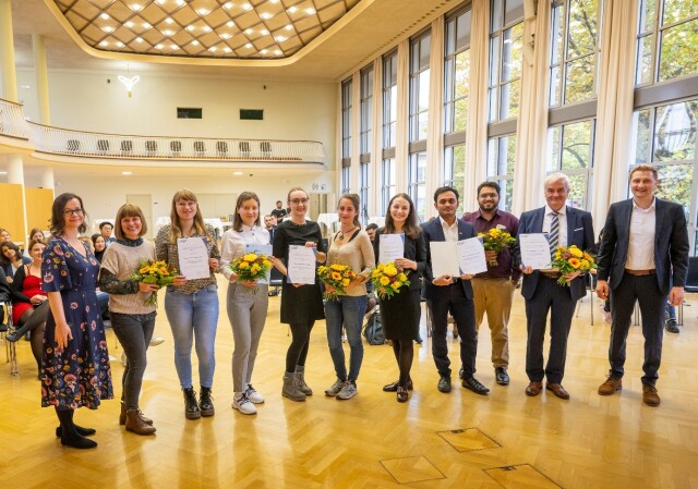 Auf dem Bild sieht man die Preisträger:innen des Preis Internationalisierung 2022 bei der Preisverleihung im Dülfersaal der TU Dresden mit Urkunden und Blumensträußen.