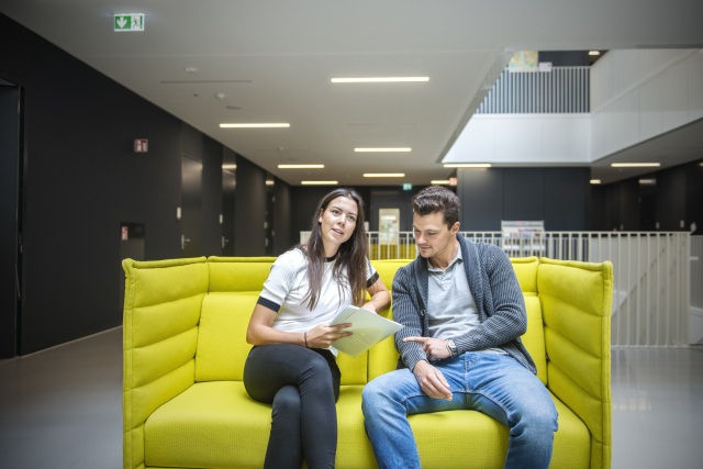 Eine Frau und ein Mann auf einem grünen Sofa, ein Paper diskutierend