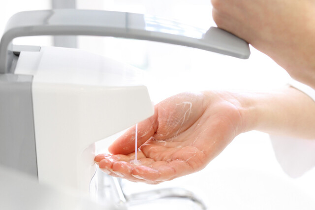 The photo shows a person washing their hands . The focus is on the soap dispenser, which is dispensing soap onto a hand.