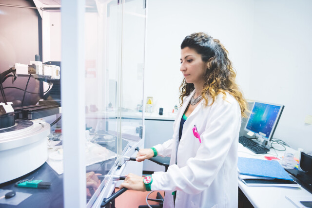 Photograph of a woman at work in a laboratory observing a piece of research equipment.