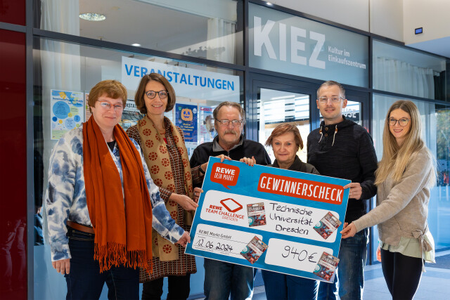The photo shows 6 people holding a large winner's check in their hands. The check reads 'Rewe Dein Markt, Rewe Team Challenge, Technische Universität Dresden, 12.06.2024, 940 €.'