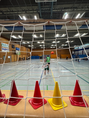 Aufnahme von hinten: Blick durch ein Handballtor in die Sporthalle hinein. Im Tor stehen Hütchen