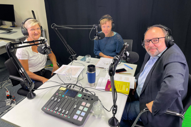 3 Personen sitzen an einem Tisch während einer Podcastaufnahme