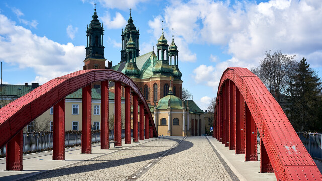 A view from a steel arch bridge towards Poznań Cathedral, with its green domes against a blue sky
