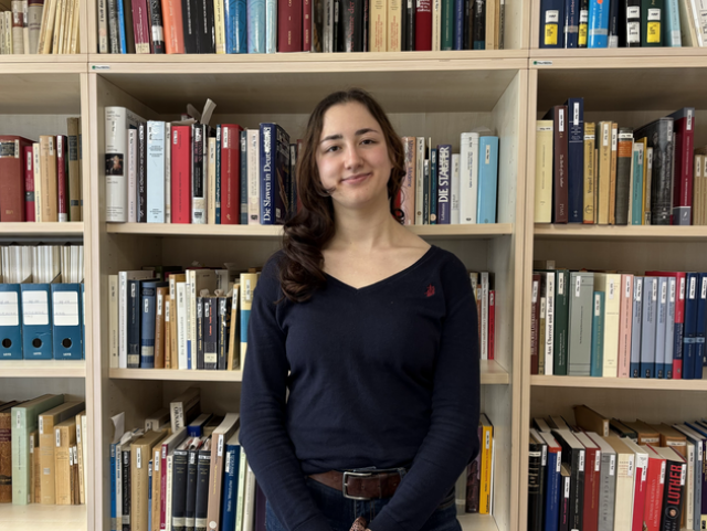 A student standing in front of a bookshelf 