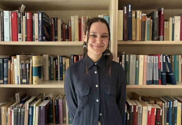 A student standing in front of a bookshelf 